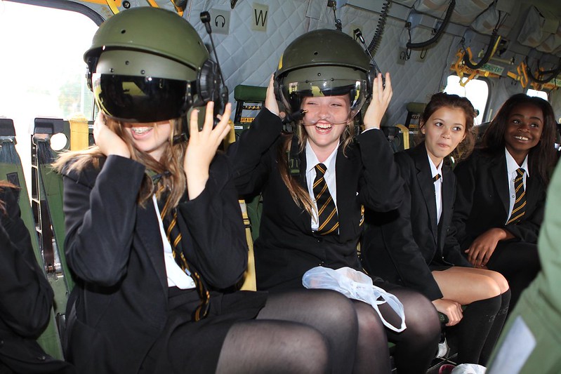 Smiling students sit in aircraft and try on flight helmets.