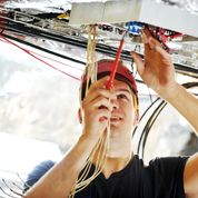 Man holds wires and manages controls in the ceiling of a boat
