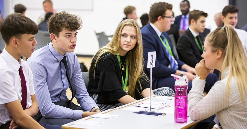 three students on one side of table talking to an adult on the other side