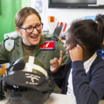 Female pilot in uniform talks with two excited students about aviation