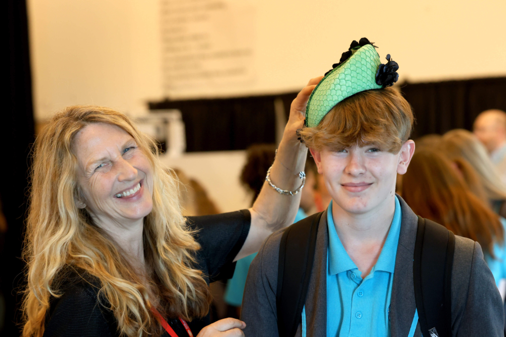 Female milliner laughing with student trying on one of her hats made from fish leather