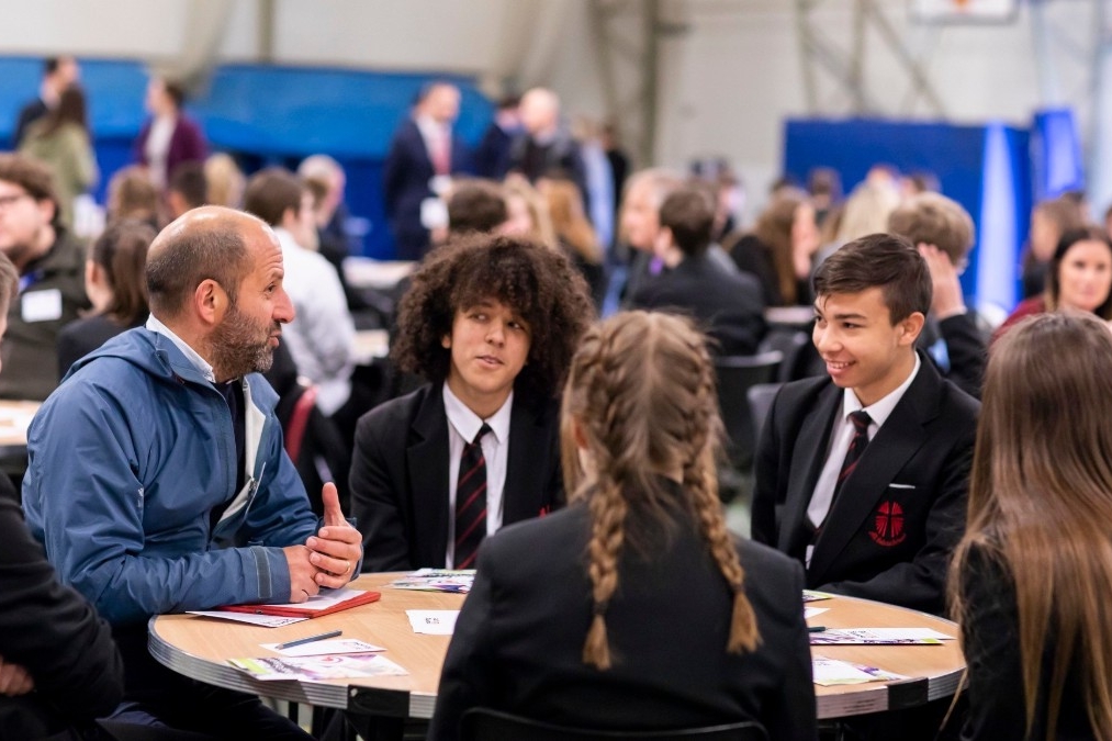 secondary pupils around a desk chatting with a volunteer