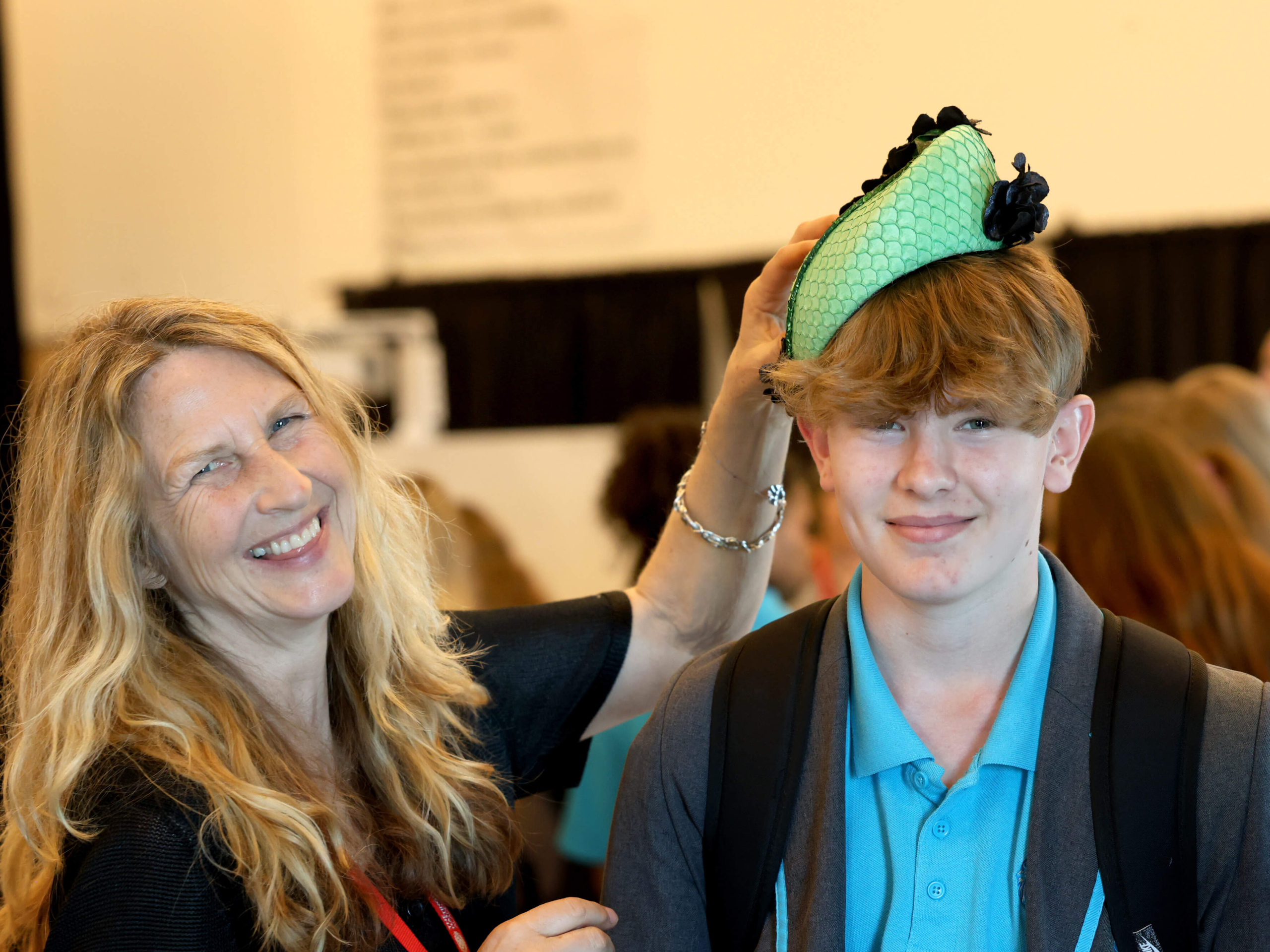 Female milliner laughing with student trying on one of her hats made from fish leather