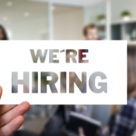 Hand holding a ‘We’re hiring’ sign in an office